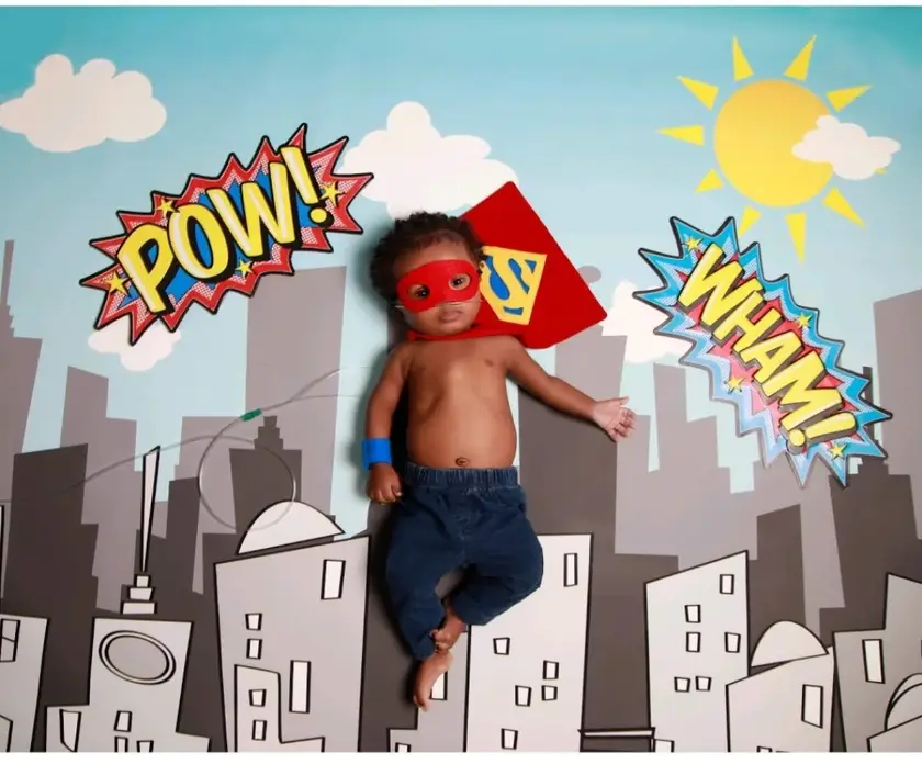 Baby Noah in a red superhero mask and cape on a comic-book backdrop