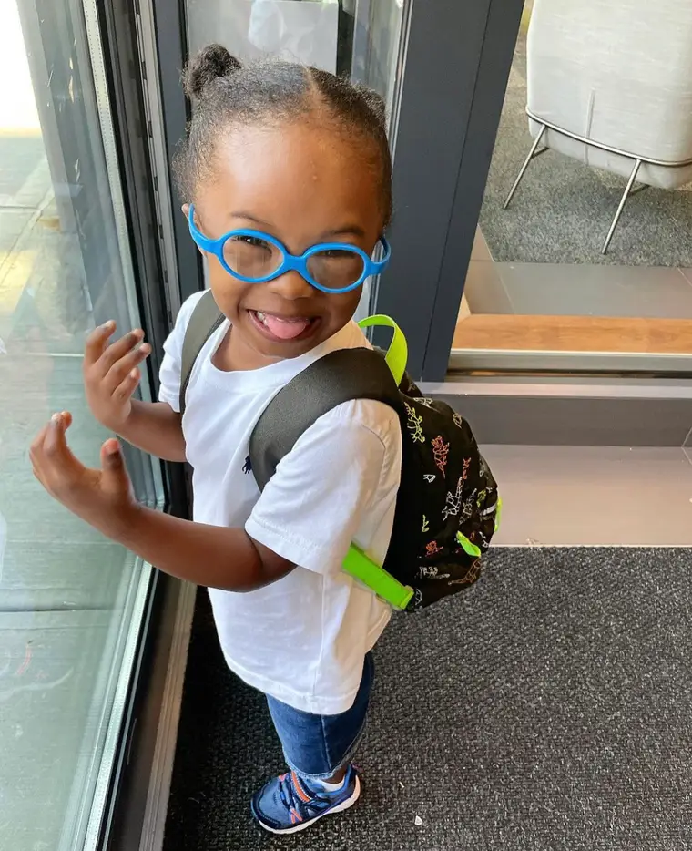 Noah, wearing bright blue glasses and a backpack, laughing on his way into school