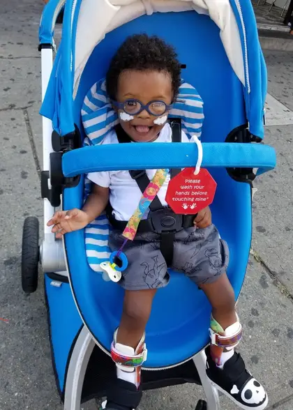 Toddler Noah laughing in a bright blue stroller on a Brooklyn sidewalk