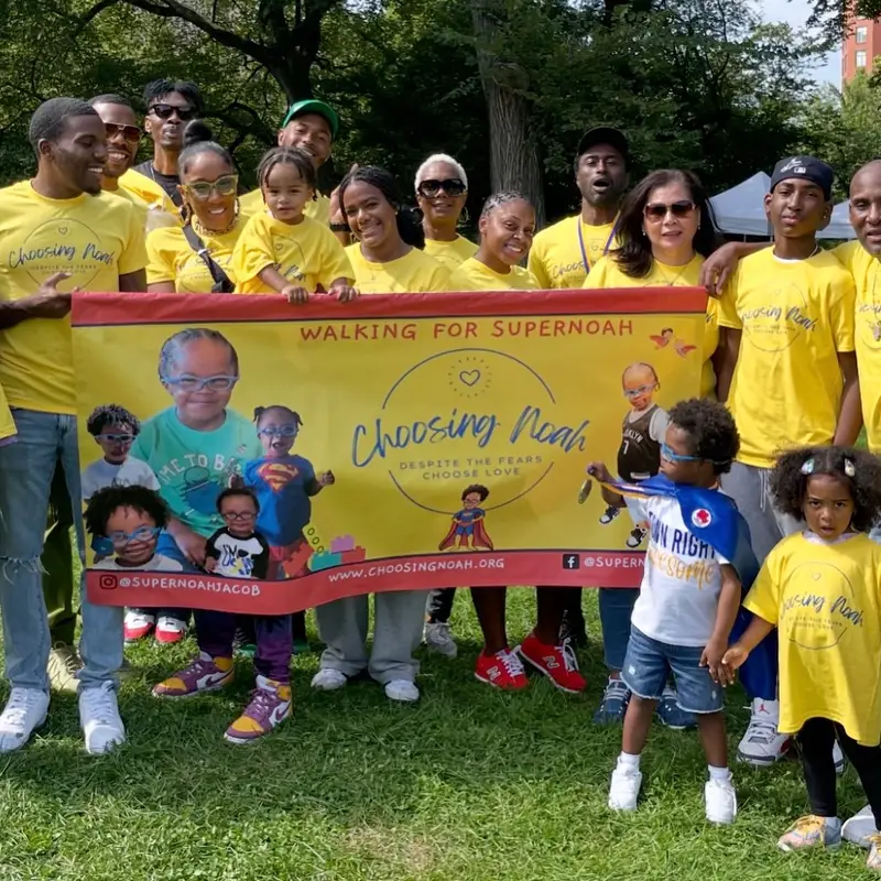 Family and friends in yellow Choosing Noah shirts holding the “Walking for Supernoah” banner in Central Park